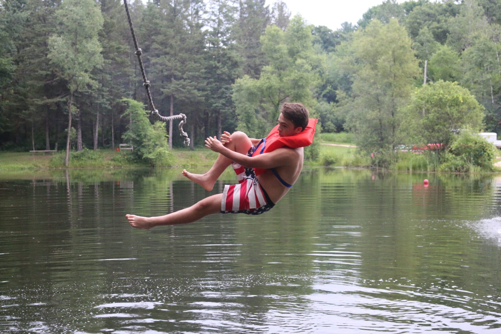 Boy camper jumping off of rope swing into lake
